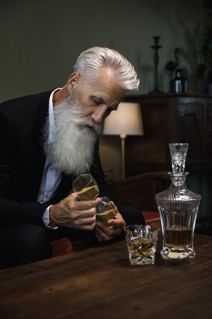 Stilvoller und gutaussehender bärtiger älterer Mann, der Whisky trinkt