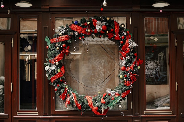 Stilvoller Weihnachtskranz mit rotem Band und Kugeln an der Gebäudehülle Moderne Weihnachtsdekoration in der Stadtstraße Winterurlaub in Europa Frohe Weihnachten und schöne Feiertage