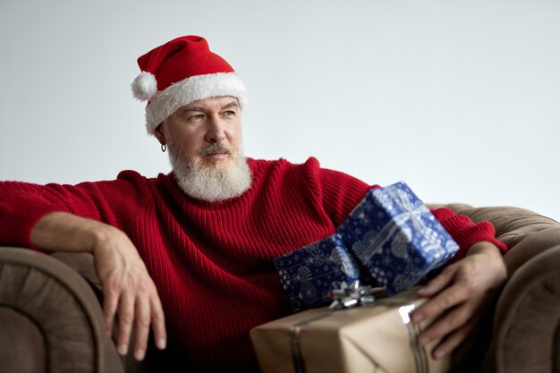 Stilvoller Weihnachtsmann mittleren Alters mit Bart mit Weihnachtsmütze und rotem Pullover, der wegschaut