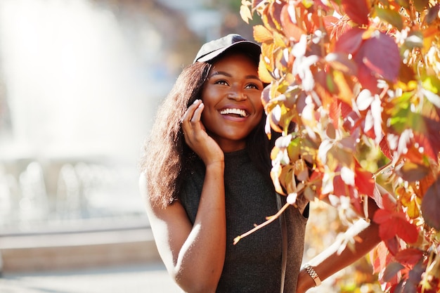 Stilvolles afrikanisch-amerikanisches Mädchen in Mütze posierte am sonnigen Herbsttag gegen rote Blätter Afrika-Modellfrau