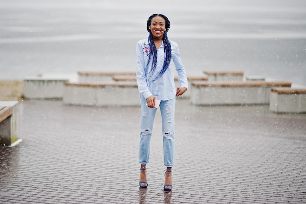 Stilvolles afrikanisch-amerikanisches Mädchen mit Dreadlocks, das bei Schneewetter im Freien ein Handy zur Hand hält