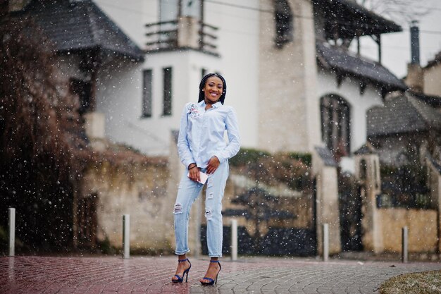 Stilvolles afrikanisch-amerikanisches Mädchen mit Dreadlocks, das bei Schneewetter im Freien ein Handy zur Hand hält