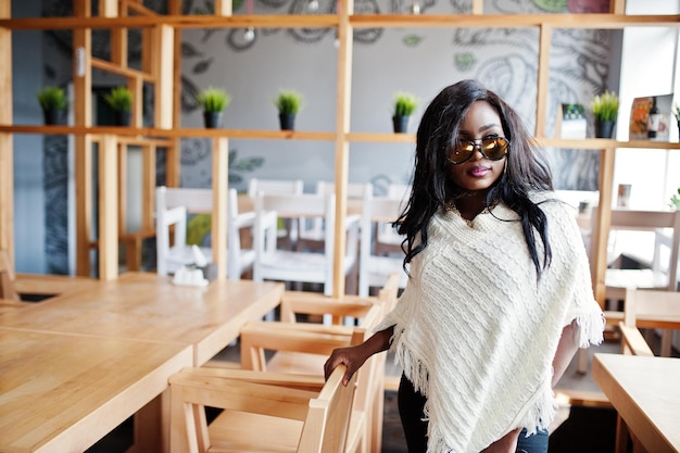 Stilvolles afrikanisch-amerikanisches Mädchen mit Sonnenbrille posierte im modernen Café