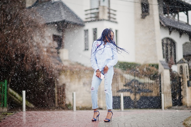 Stilvolles Afroamerikanermädchen mit den Furcht, die Handy zur Hand, Schneewetter im Freien halten.