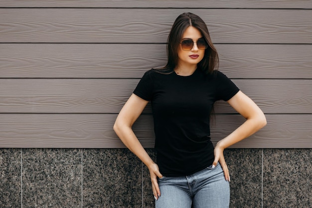 Foto stilvolles brünettes mädchen mit schwarzem t-shirt und brille, das gegen den städtischen kleidungsstil der straße posiert