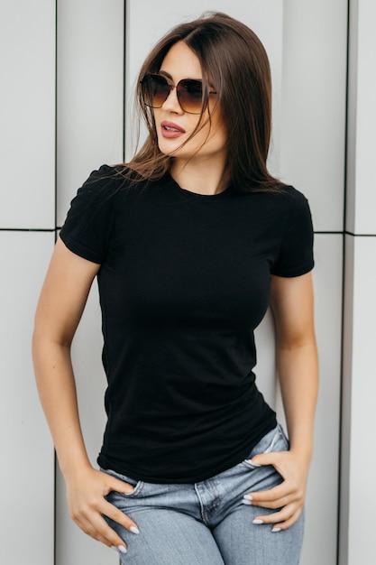 Stilvolles brünettes Mädchen mit schwarzem T-Shirt und Brille, das gegen den städtischen Kleidungsstil der Straße posiert