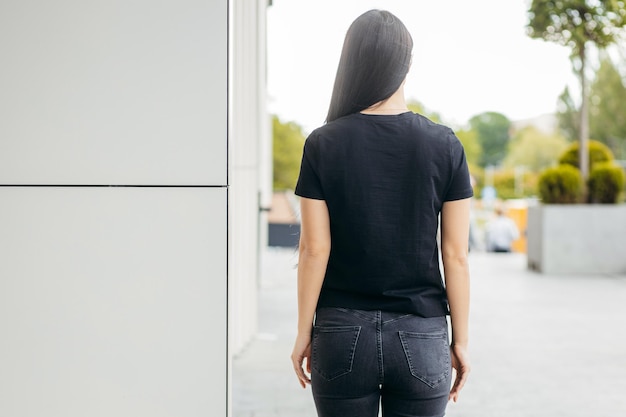 Stilvolles brünettes Mädchen mit schwarzem T-Shirt und Jeans, das gegen den urbanen Kleidungsstil der Straße posiert