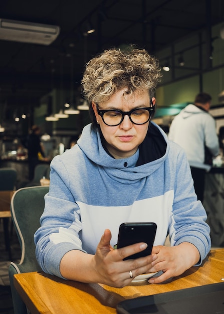 Stilvolles Frauen-Freizeitporträt im öffentlichen Café, das mit dem Handy arbeitet