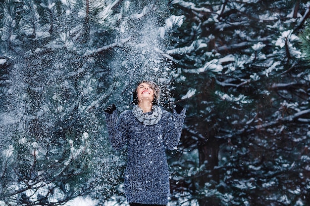 Stilvolles fröhliches Mädchen in einem Pullover im Winterwald Schnee vom Baum fällt auf das Mädchen