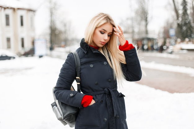 Stilvolles glamouröses junges Modellmädchen in einem Modewintermantel mit einer Tasche, die in der Stadt geht