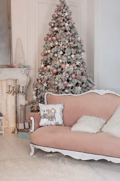 Stilvolles Interieur des Wohnzimmers mit Weihnachtsbaum und leuchtenden Girlanden und Komfortsofa