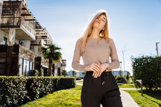 Stilvolles junges blondes Mädchen, das draußen in der Sonne aufwirft, Straßenstil