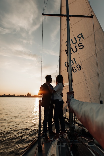 Stilvolles junges Paar bei Sonnenuntergang auf einer Yacht, die auf einer Yacht auf dem Wasser segelt