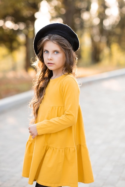 Stilvolles Kind Mädchen 56 Jahre alt tragen gelbes Kleid und Baskenmütze im Herbst Park im Freien Blick in die Kamera Herbstsaison Kindheit