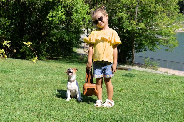 Stilvolles kleines Mädchen, das mit ihrem Hund Jack Russell Terrier im Park spielt