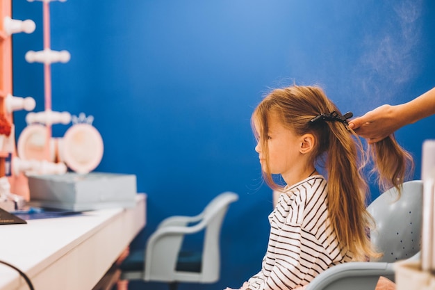 Stilvolles kleines Mädchen in einem Schönheitssalon für Kinder, wo sie eine schöne Frisur machte Stylistin macht kleine Mädchen stilvolle Frisur