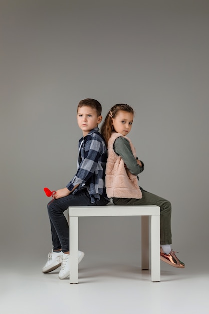 Stilvolles kleines Paar Kind Mädchen und Junge mit roten Herzen auf Stick in modischen Kleidern sitzen zusammen