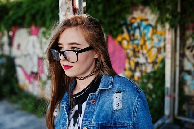 Stilvolles, lässiges Hipster-Mädchen in Jeans und Brille an einer großen Graffiti-Wand