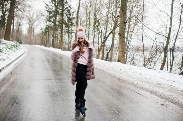 Stilvolles Mädchen in Pelzmantel und Kopfbedeckung am Wintertag auf der Straße.