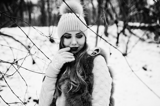 Stilvolles Mädchen in Pelzmantel und Kopfbedeckung im Winterwald.