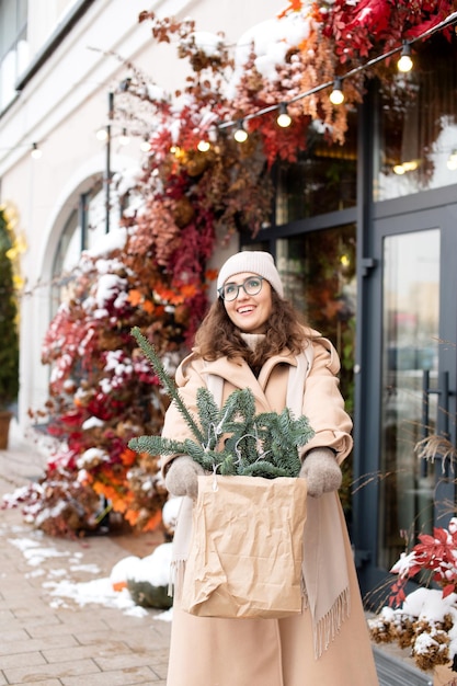 Stilvolles Mädchen mit Brille freut sich, Weihnachtsnobilis in der Stadt zu kaufen