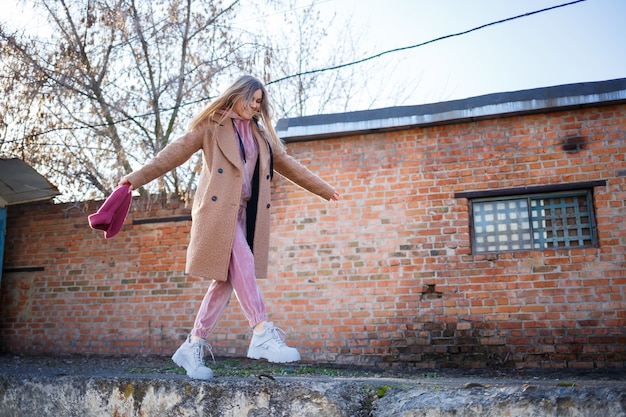 Stilvolles Mädchenmodell in braunem Mantel, rosa Anzug und grauen Stiefeln auf den Ruinen der Stadt. Die Trends der modernen Mode. Modisches Bild