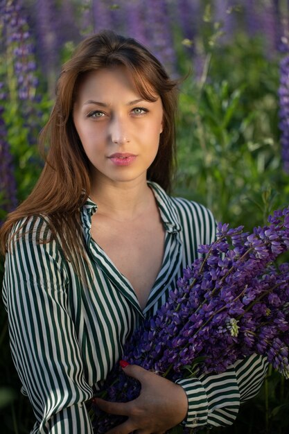 Stilvolles nachdenkliches Mädchen im gestreiften Kleid, das mit Handvoll Lupinenblumen aufwirft