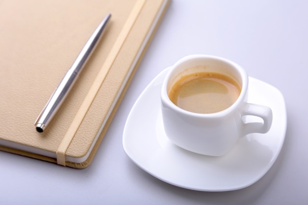 Foto stilvolles notizbuch, kugelschreiber und weiße tasse mit einem duftenden espresso auf dem schreibtisch.