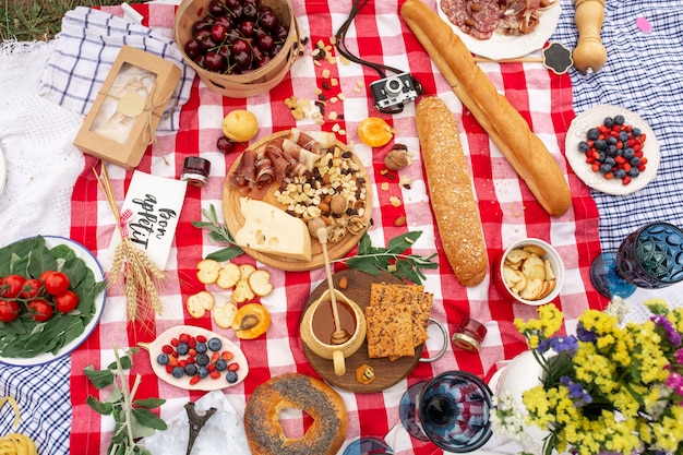 Stilvolles Picknick auf dem grünen Rasen. Frische Hörnchen und eine Teekanne mit Tee auf einer Bettdecke nahe einem aus Weiden geflochtenen weiblichen Hut. Instagram-Inhalt