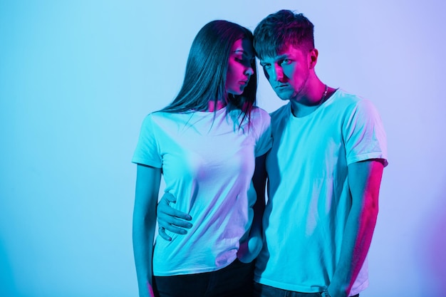 Stilvolles, schönes junges Paar in weißen T-Shirts mit Neon- und Rosalicht im Studio. Hübsches Mädchenmodell und gutaussehender Mann mit farbigem Hintergrund