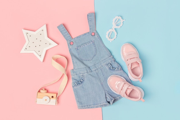 Stilvolles Sommerset mit Kinderkleidung Denim-Jumpsuit rosa Turnschuhe und Accessoires auf rosa-blauem Hintergrund Fashion Girl Lookbook-Konzept Draufsicht Flache Lage