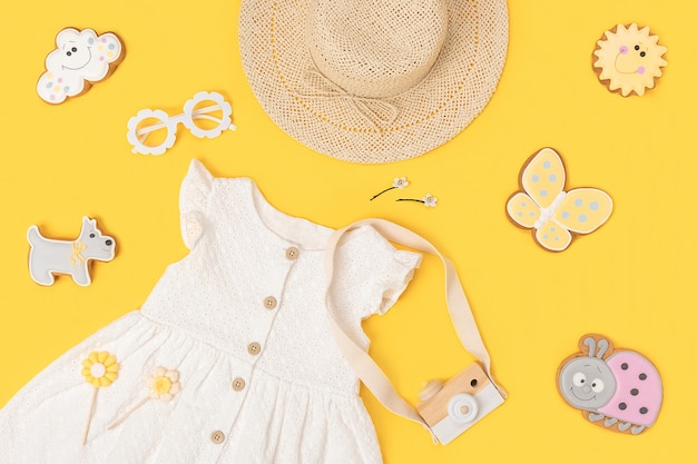Stilvolles Sommerset mit Kinderkleidung. Weißes Kleid, Strohhut, Sonnenbrille und Accessoires auf gelbem Hintergrund. Mode Mädchen Lookbook-Konzept. Ansicht von oben Flach legen.