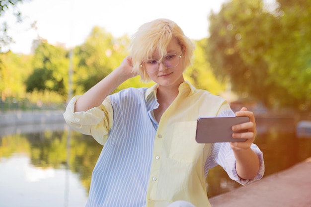 Stilvolles Teenager-Mädchen, das draußen ein Selfie machtSonnenlicht im Hintergrund