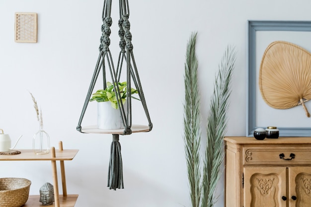 Foto stilvolles und boho-interieur des offenen raums mit holzschreibtisch, stuhl, lampe und weißem regal. design und elegante persönliche accessoires. botanik und minimalistisch. wohnkultur. abstraktes gemälde an der wand