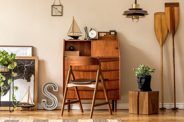 Stilvolles und Vintage-Innendesign des offenen Raums mit Retro-Holzschrank, Designstuhl, Karten, Paddel, Schiff, Kakteen, Pflanzen und eleganten persönlichen Accessoires. Moderne Vintage-Wohnkultur.