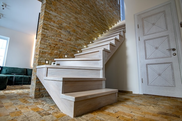 Stilvolles zeitgenössisches Holztreppenhaus im Dachbodenhausinnenraum. Moderner Flur mit dekorativen Kalksteinwänden und weißen Eichentreppen.