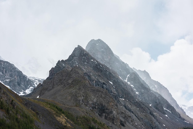 Stimmungsvolle Berglandschaft mit großem spitzen Gipfel unter grauem, wolkigem Himmel. Düstere Landschaft mit hohem, spitzen Berggipfel mit scharfen Felsen in niedrigen Wolken. Riesige felsige Spitze bei Regenwetter