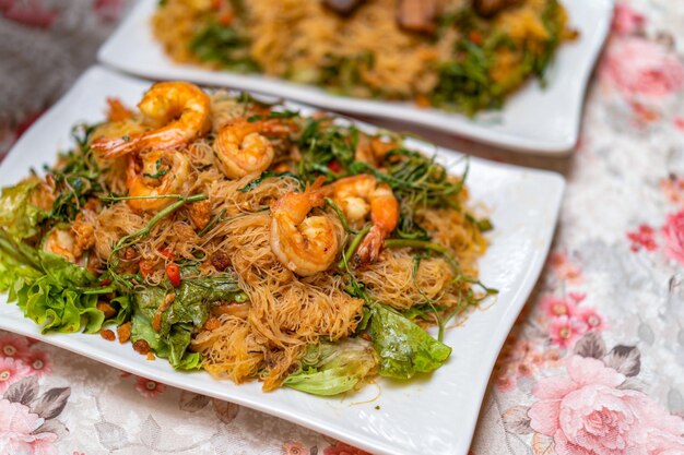 Stir Fried Rice Vermicelli com Water Minosa e Camarões em prato retangular branco na tampa da mesa de flores rosa