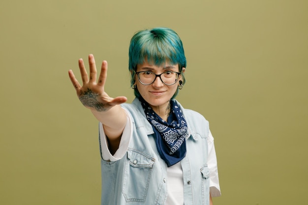 Stirnrunzelnde junge Frau mit Brille Bandana am Hals, die in die Kamera blickt und fünf mit der Hand isoliert auf olivgrünem Hintergrund zeigt