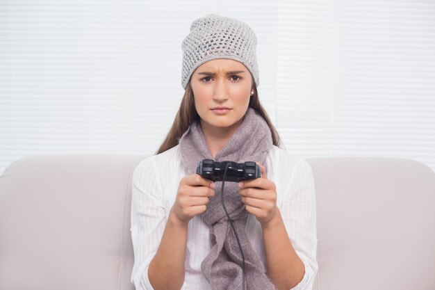 Stirnrunzelnder Brunette mit Winterhut auf dem Spielen von Videospielen