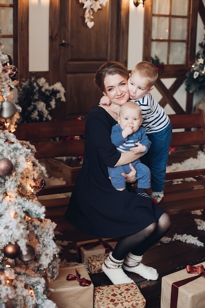 Stock Foto der schönen lächelnden Mutter, die kleines Baby und ihren älteren Sohn hält, umarmt sie