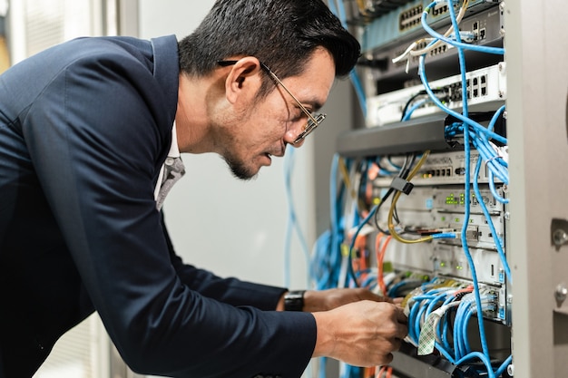 Stock Foto eines jungen Netzwerktechnikers, der Tablet hält, um Netzwerkkabel im Serverschrank im Netzwerkserverraum anzuschließen. IT-Ingenieur, der im Netzwerkserverraum arbeitet