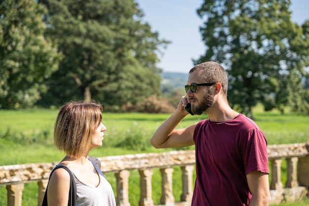 Stock Foto eines Paares, das mit dem Handy spricht und sich in einem Garten mit einem Marmorgeländer ansieht. Lebensstil