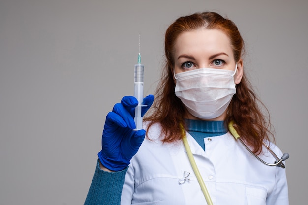 Stock Foto Porträt eines rothaarigen professionellen Wissenschaftlers in Schutzmaske, weißem Mantel und Handschuh halten eine Spritze mit Impfstoff gegen Virus oder Grippe gefüllt