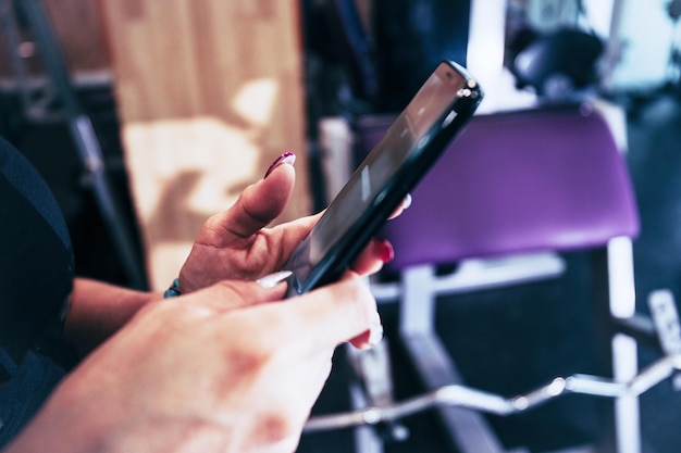 Stock Foto von einem Detail der Hände eines Mädchens, die ein Handy in einem Fitnessstudio halten Sport und Freizeit