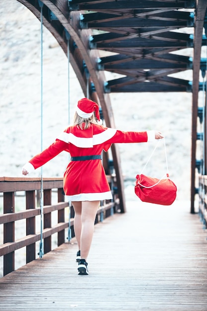 Stock Foto von Mama Noel, die mit einer roten Tasche in der Hand auf einer Holzbrücke rückwärts geht