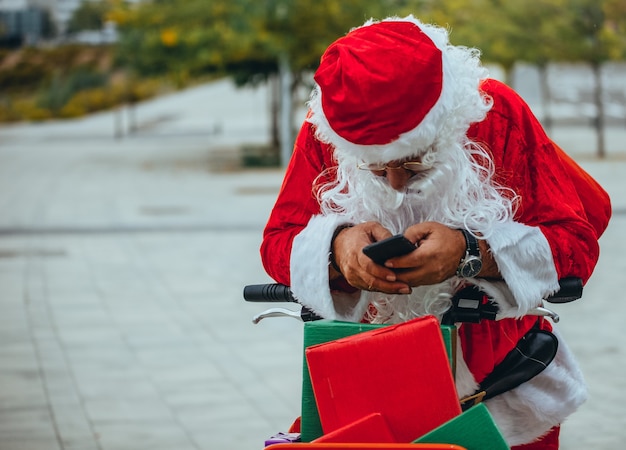 Stock photo de santa claus hablando con un teléfono móvil con un parque detrás de desenfocado