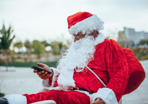 Stock photo de santa claus hablando con un teléfono móvil con un parque detrás de desenfocado