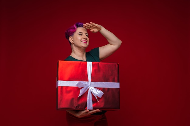 Stockfoto der fröhlichen erwachsenen Frau mit dem kurzen gefärbten Haar, das Weihnachts-T-Shirt trägt, Stapel von schönen eingewickelten Weihnachtsgeschenken in den Händen hält und lächelt