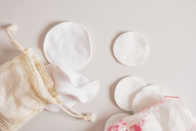 Stoff- und Wattepads zum Reinigen der Haut von Make-up, ein Netzbeutel und ein Plastikbeutel zum Aufbewahren auf beigem Hintergrund Zero Waste, Mehrweg, Öko, Make-up-Entferner und Waschkonzept.